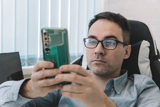 Smiling businessman with eyesight problems, he is adjusting his glasses and reading something on his mobile phone