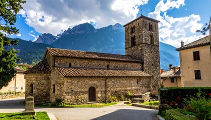 Fototapeta premium Ancient stone church with a tall tower set amidst verdant greenery and majestic mountain peaks