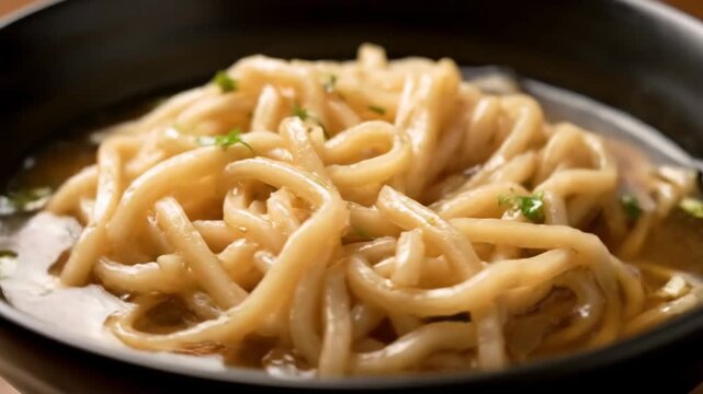 Close-up of thick asian noodles (udon or ramen) in a savory broth, garnished with fresh herbs, served hot in a black bowl. appetizing comfort food.