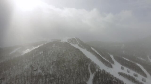 Aerial view of a snowy mountain with ski slopes under a bright sky with dramatic clouds and light rays