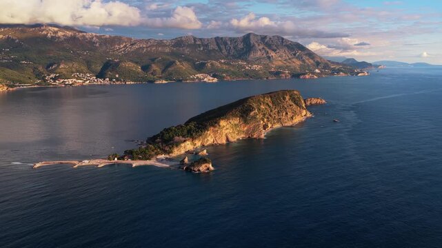 Aerial view of Saint Nicholas island and Budva coast at sunset, slow motion drone flight.