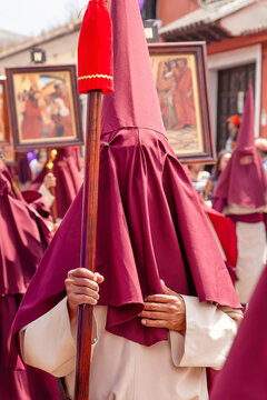 Hooded cucurucho in traditional robe carrying staff during Holy Week procession in Antigua Guatemala, representing Catholic religious tradition and cultural heritage