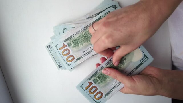 Hands counting a large stack of one hundred dollar bills on a white table, financial success concept.