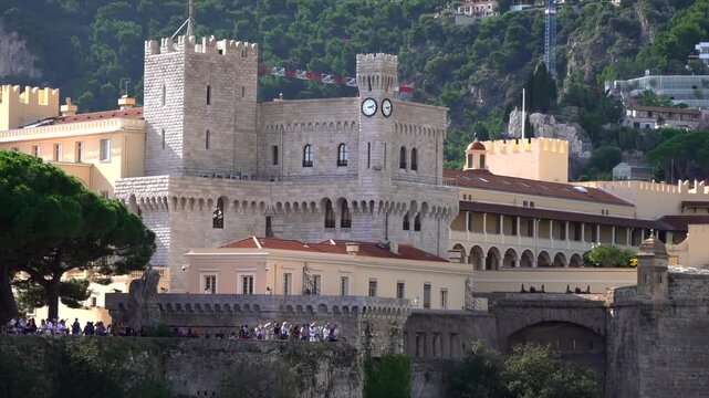 People walking on ancient fortress wall in monaco monte carlo, historic stone castle with clock tower.