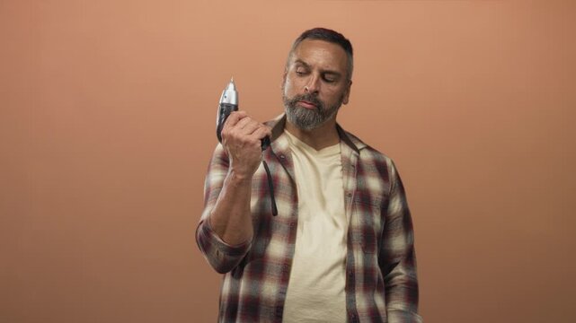 Man holding a power drill, hand gripping the tool in a studio with terracotta wall; confidence craftsmanship.