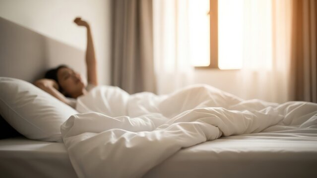 Person waking up in a bright bedroom, stretching under white bedding near a sunny window