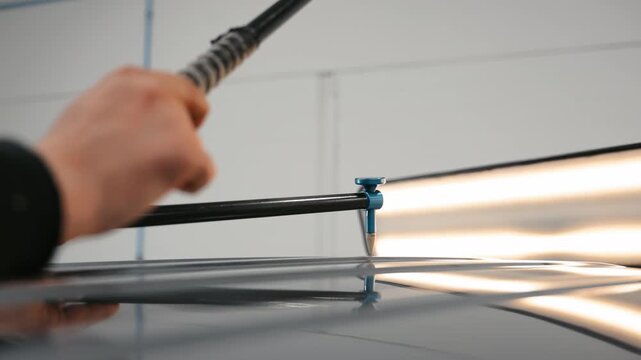 Process of PDR pointless dent repair on car body, mechanic at the auto shop with tools to repair dents in damaged car body after hail