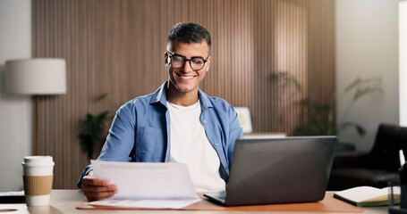 Fototapeta premium Man, smile and document in home with laptop, remote work and proposal for digital marketing campaign. Person, paperwork and computer in house with idea, creativity and plan for freelance advertising.