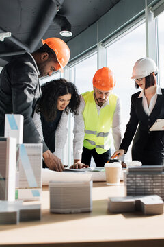 A diverse group of architects and engineers collaborate on blueprints and building models in a modern office setting