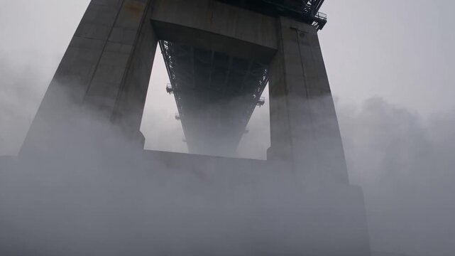 Foggy urban monument. Large concrete structure pierces through heavy fog with textured details. Tall concrete bridge looms with imposing presence amid thick fog and atmospheric urban setting