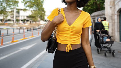 Obraz premium Young woman walks along city street wearing yellow shirt and black skirt in summer sun