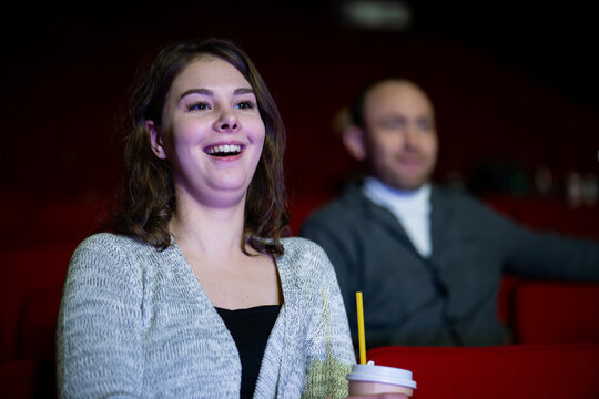 smiling woman with popcorn watches a movie in a cinema, enjoying a comedy or humorous film.