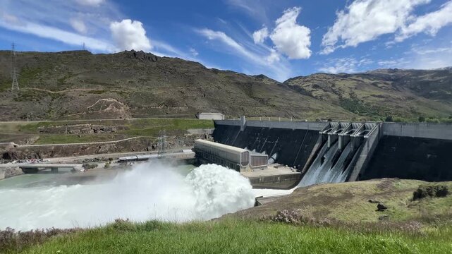 Clyde Dam in New Zealand with spillway gates fully open, releasing large volumes of turbulent white water into the Clutha River below
