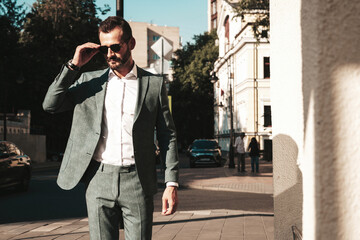 Fototapeta premium Portrait of handsome confident stylish hipster lambersexual model.Modern man dressed in elegant suit. Fashion male posing in the street background in Europe city at sunset. In sunglasses