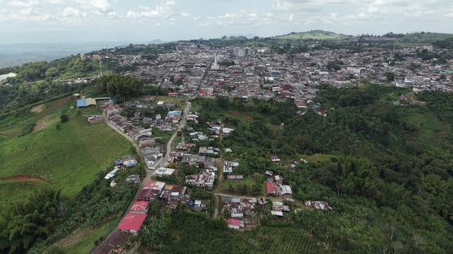 A breathtaking aerial footage showcasing the lush hills and vibrant homes of Valle del Cauca, Colombia, under a vivid blue sky, capturing a serene and picturesque rural landscape.