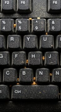 Dusty black keyboard with crumbs lodged between keys