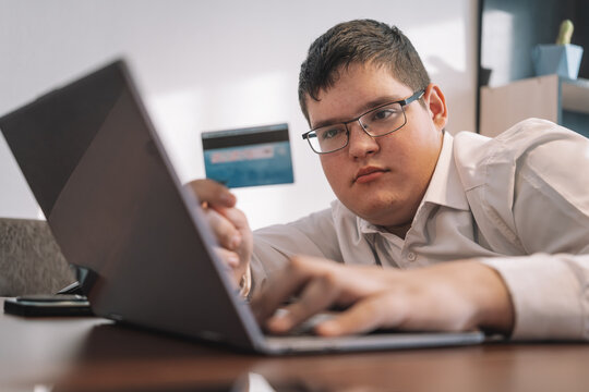 Children sitting in the office and working on a laptop. teen boy buys on the Internet. Young buyer pays by credit card.