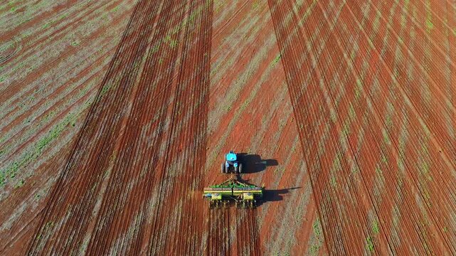 Drone tracking shot of tractor with seed drill in agribusiness land preparation in Formosa, Goi&aacute;s, Brazil, showing precision row planting on cultivated soil in central-west farming region
