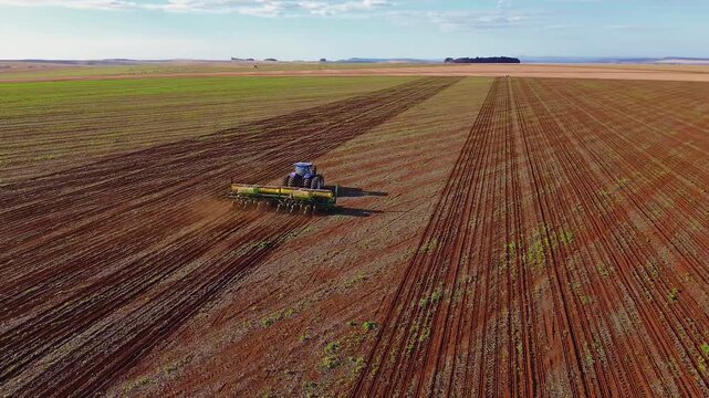 Soybean planting advances with tractor pulling wide row crop planter equipped with seed meters fertilizer tanks and GPS auto steer across structured soil rows in Formosa Goias Brazil, aerial tracking