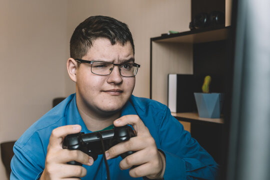 teenager in glasses sits at a computer holding a joystick, his face focused but sad, expressing disappointment after losing a video game.