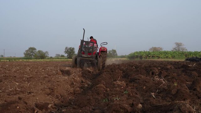 Indian farmer working or plowing agriculture field with tractor 