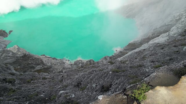 Scenic aerial view of Kawah Ijen volcano crater with turquoise lake and sulfur smoke in East Java Indonesia under blue sky
