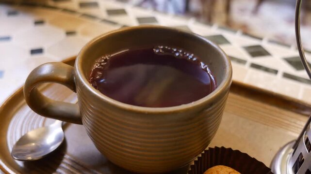 Cinematic shot of hand picking up steaming cup of hot berry tea from wooden tray in cozy cafe setting.
