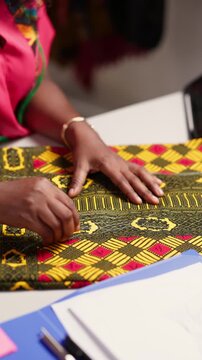 Vertical video, African tailor's hands marking colorful ankara fabric with chalk on a workspace