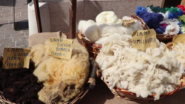 Baskets filled with raw and semi-washed sheep and alpaca wool displayed at a medieval historical market in Italy.