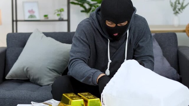 Masked Robber Counting Stolen Cash and Gold Bars on Living Room Sofa