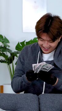 Criminal in Black Gloves Counting Stolen Cash Behind a Sofa