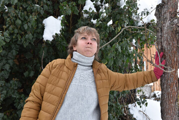 Woman in mustard puffer jacket leaning against a tree in the snow © salajean