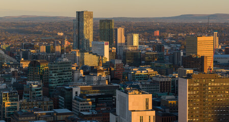 Obraz premium A wide aerial panorama of Manchester city centre at sunrise, featuring modern skyscrapers and office buildings glowing under a golden morning sky.