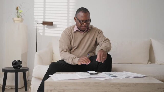 Man distributing money for monthly payments, putting banknotes on utility bills. Serious african american male person counting dollars cash and spreading incomes, accountant planning of family budget