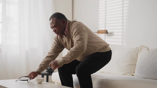 Senior black man feeling lower back pain, radiculitis, disease of old age. African american male person sitting on couch in living room and suffering of backache, aging and healthcare, stay active
