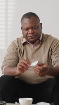 African american man using nicotine patch, fixing on arm skin, vertical portrait at home. Modern transdermal patch for curing nicotine addiction and inputting medicine in blood, modern technology
