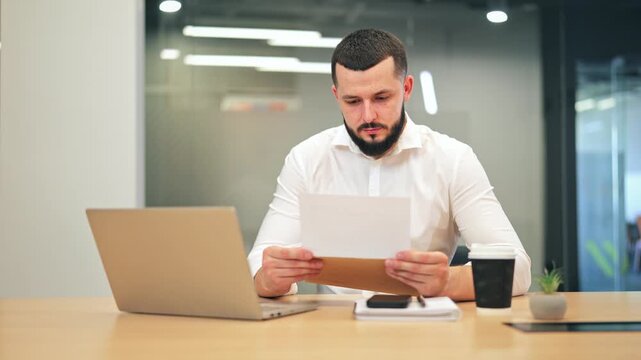 Professional in modern office reads document, experiencing surprise and happiness. Good news brings joy and excitement, signaling success and positive achievement in business endeavors.