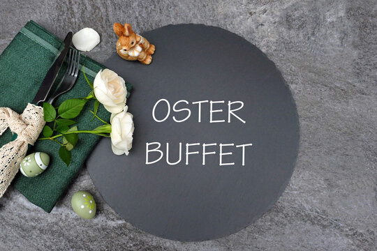 Tischdekoration zu Ostern. Modernes Osterbuffet-Gedeck auf Schieferplatte mit wei&szlig;en Rosen und dunkelgr&uuml;ner Serviette.