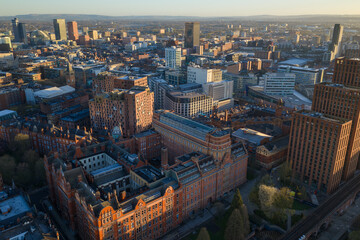 Obraz premium Aerial perspective of Manchester at sunrise, showing the sun's glow on the historic terracotta architecture and the expanding city skyline.