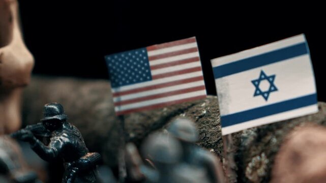 Miniature toy soldiers in a war scene with american and israeli flags. A human skull ominously looms over the battlefield diorama