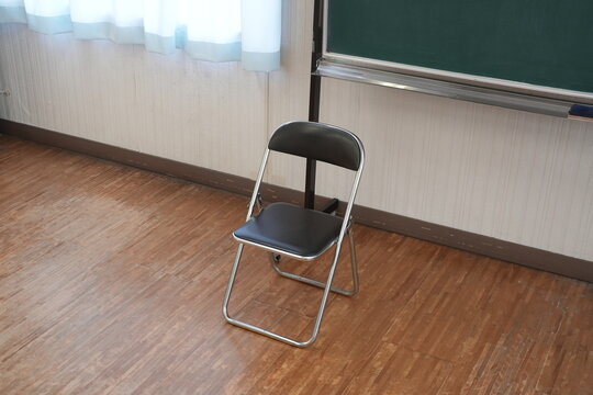 Empty chair sits beside green chalkboard. Wooden floor reflects soft daylight from window. Curtains filter gentle, even illumination. No people, no movement-stillness dominates space