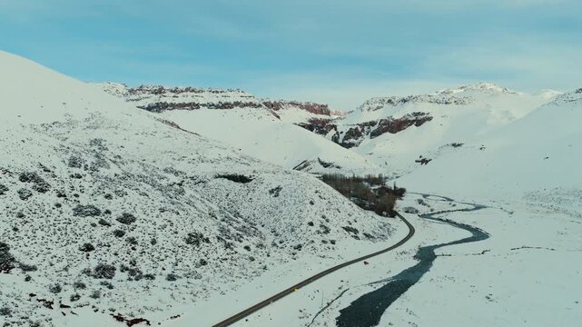 Ruta Nacional 145 follows R&iacute;o Chico through snow covered Andean valley in Paso Pehuenche Las Loicas Malargue Mendoza Argentina within R&iacute;o Grande basin near Chile border crossing, aerial follow shot