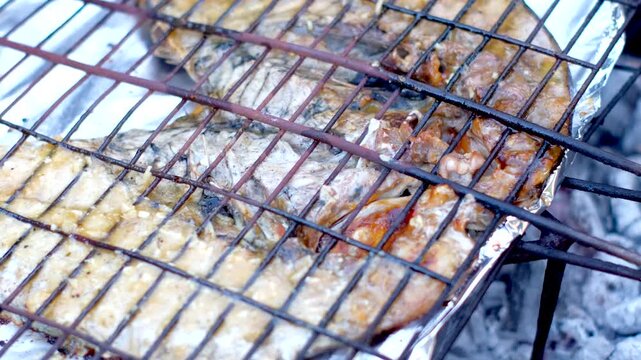 Juicy black bream fish on grid being grilled on hot coals, close-up view