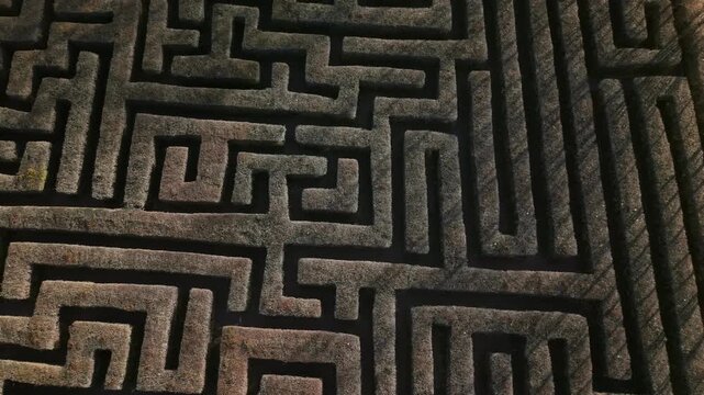 Geometric hedge maze pattern with narrow paths and dense trimmed hedges, drone top down tracking pan