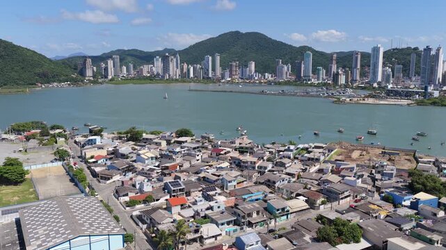Itajai city along the Itajai Acu River with dense residential foreground, urban skyline and Morro da Cruz hill in Santa Catarina, South Brazil, coastal city landscape, aerial view, drone ascent, high