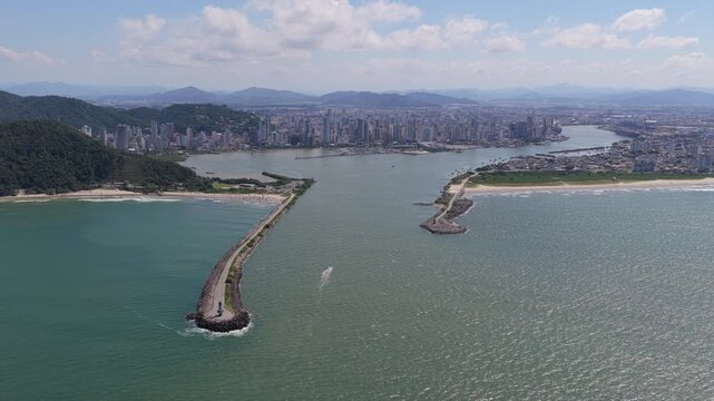 Aerial view of Itajai harbor entrance at the Itajai Acu River mouth in Santa Catarina, Brazil, showing breakwaters, coastal cityscape and Atlantic shoreline with navigation channel.