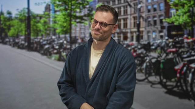 Man wearing robe and glasses pointing with right hand toward bicycles on a crowded street in front of brick buildings, slight smile and folded left arm; amused nonchalance.