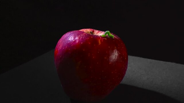Tiny green inchworm crawling on the surface of a fresh red apple, a conceptual representation of nature's simple processes, healthy organic food, and the cycle of life on a dark background