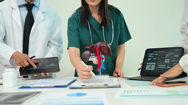 Medical team having a meeting with doctors in white lab coats and surgical scrubs seated at a table discussing a patients working online using computers in the medical industry