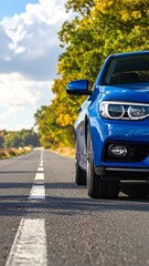 Fototapeta premium A blue car driving on an asphalt road lined with trees